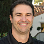 A man smiling for the camera in front of a building.